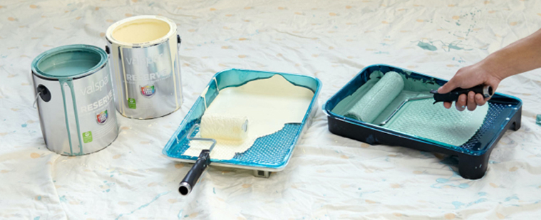 Hand pushing a roller in paint tray with a second tray next to it and two open cans.