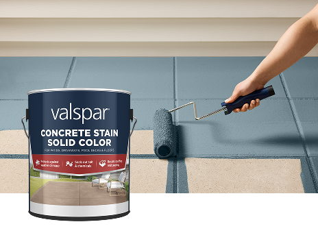 Valspar Solid Color Concrete Stain can displayed beside a paint roller coating a concrete surface in Cottage Door blue-gray, demonstrating durable color protection for patios, walkways, and outdoor living spaces.