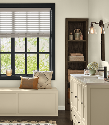Bathroom with window, vanity, light fixtures, drawer with pillows on it, shelf with towels and candle on window sill. 