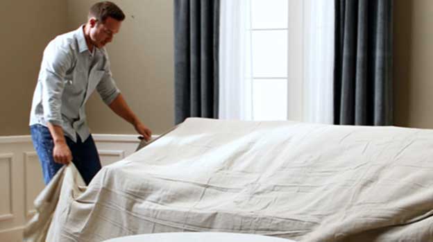 Man covering sofa to protect it in preparation for painting.